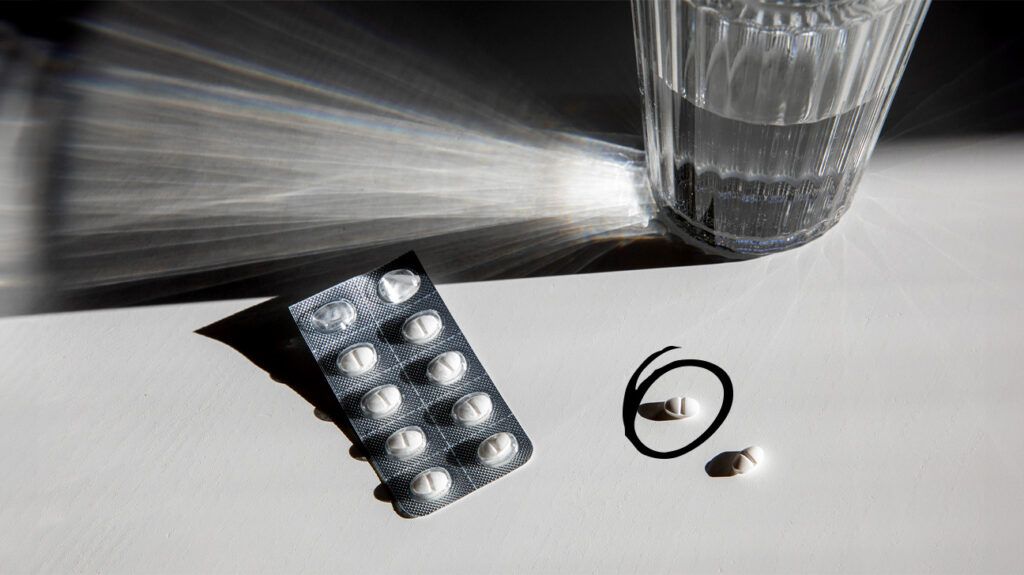 black and white photo of capsule blister pack and glass of water