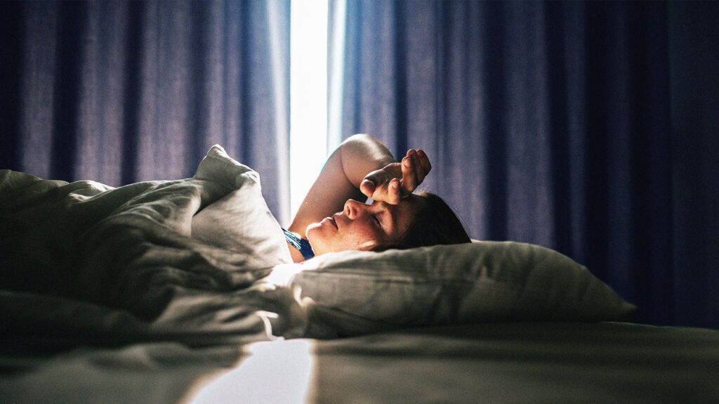 Female lying in bed with her eyes closed and hand on her forehead