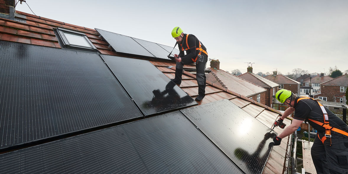 Two people installing solar panels on a pitched roof