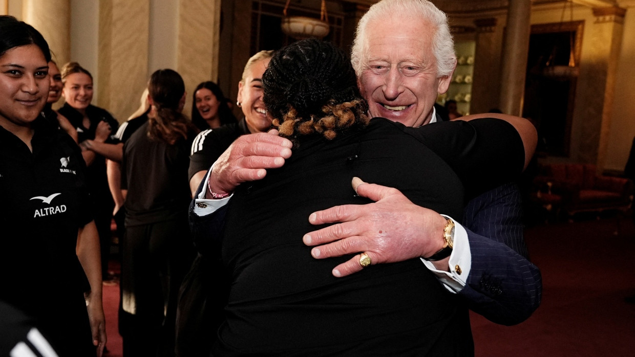 König Charles III. umarmt eine neuseeländische Rugby-Spielerin im Buckingham Palace in London.