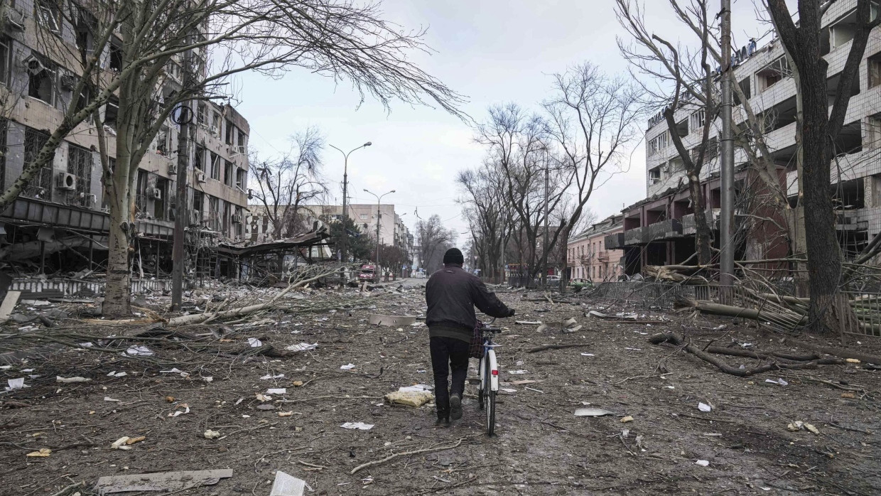 Ein Mann geht mit einem Fahrrad in einer durch Beschuss beschädigten Straße in Mariupol.