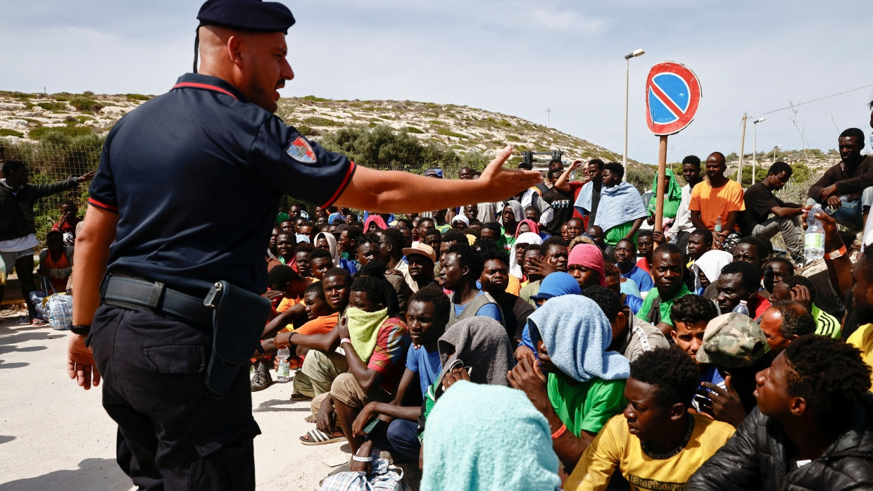 Ein italienischer Polizist gestikuliert mit einigen Migranten nach deren Ankunft auf Lampedusa