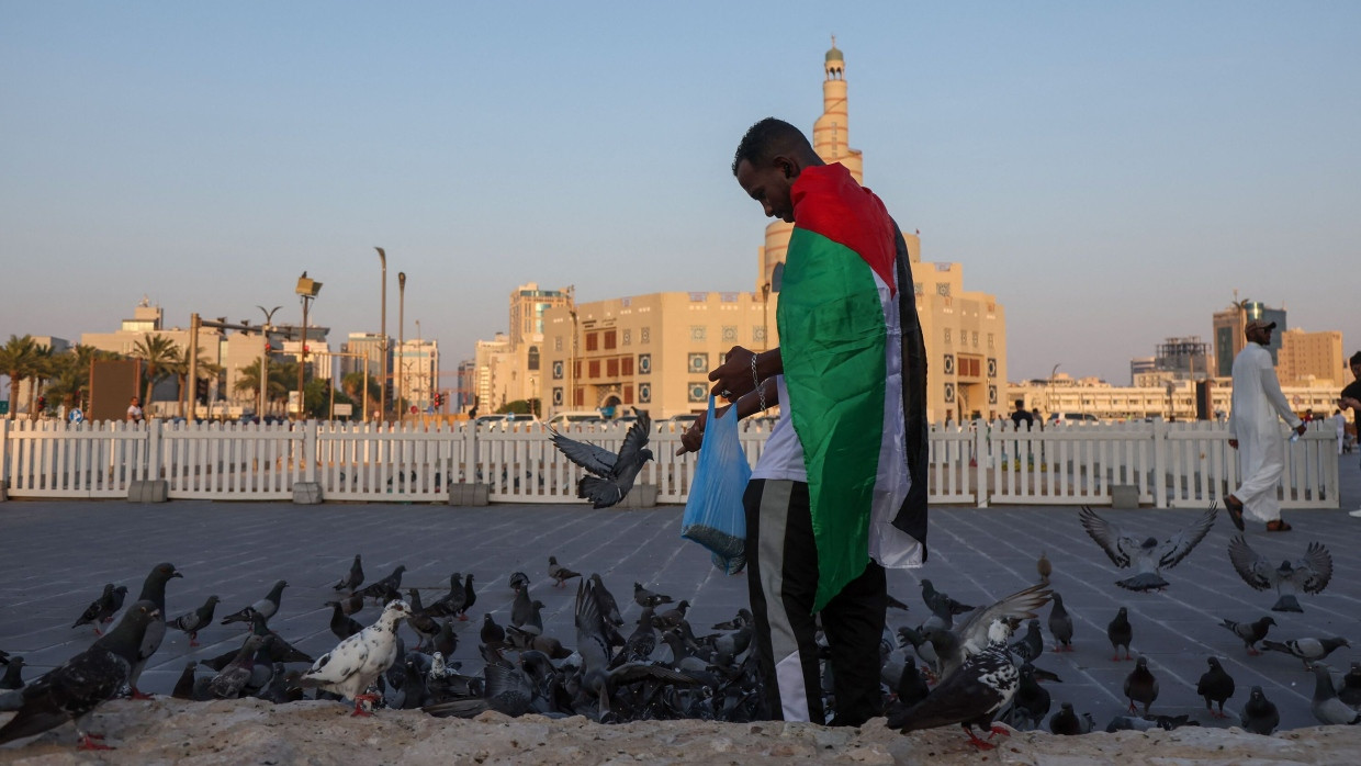 Vor der Fanar Moschee in Doha füttert ein Mann mit palästinensischer Flagge Tauben, 16.8.2024.