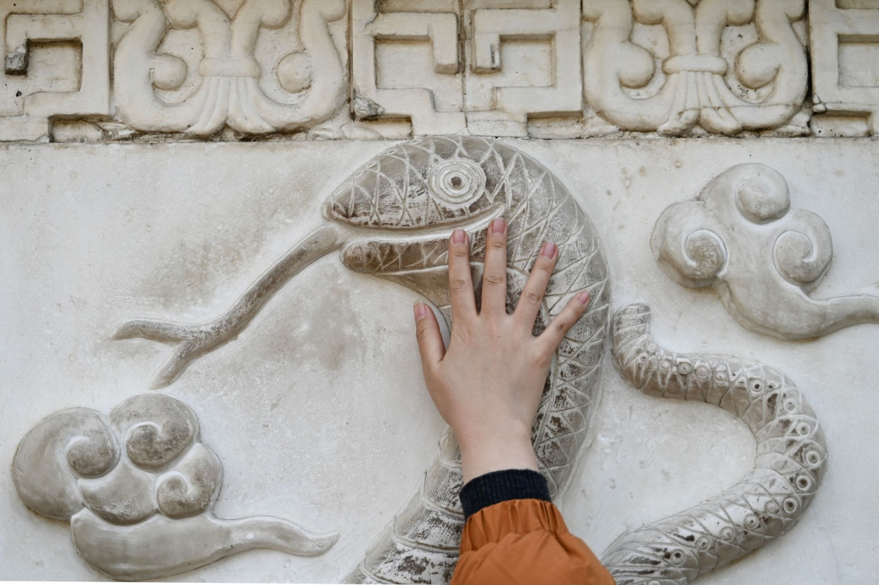 Ein Mann berührt die Schlangenfigur auf der Steinmauer, die Tiere im chinesischen Tierkreis darstellt, im taoistischen Baiyun-Tempel, auch bekannt als der Tempel der Weißen Wolken in Peking.