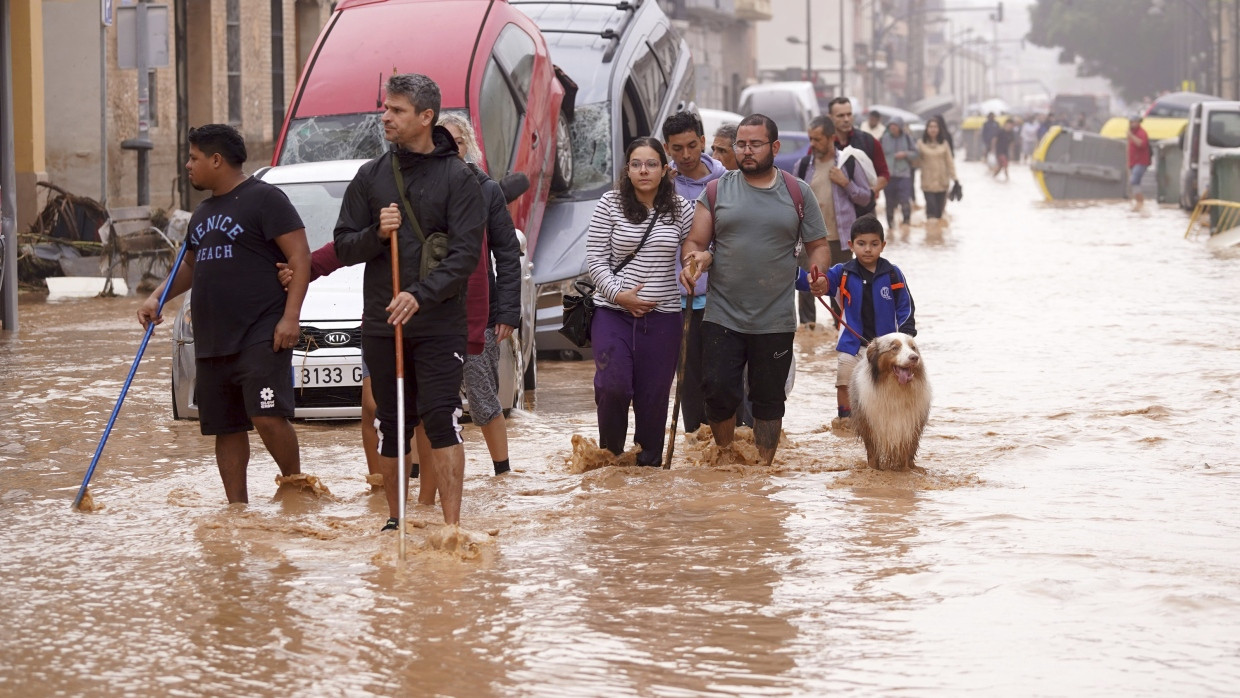 Spanien, Valencia: Menschen gehen durch überflutete Straßen an Autos vorbei, die von den Wassermassen übereinander geschoben wurden.