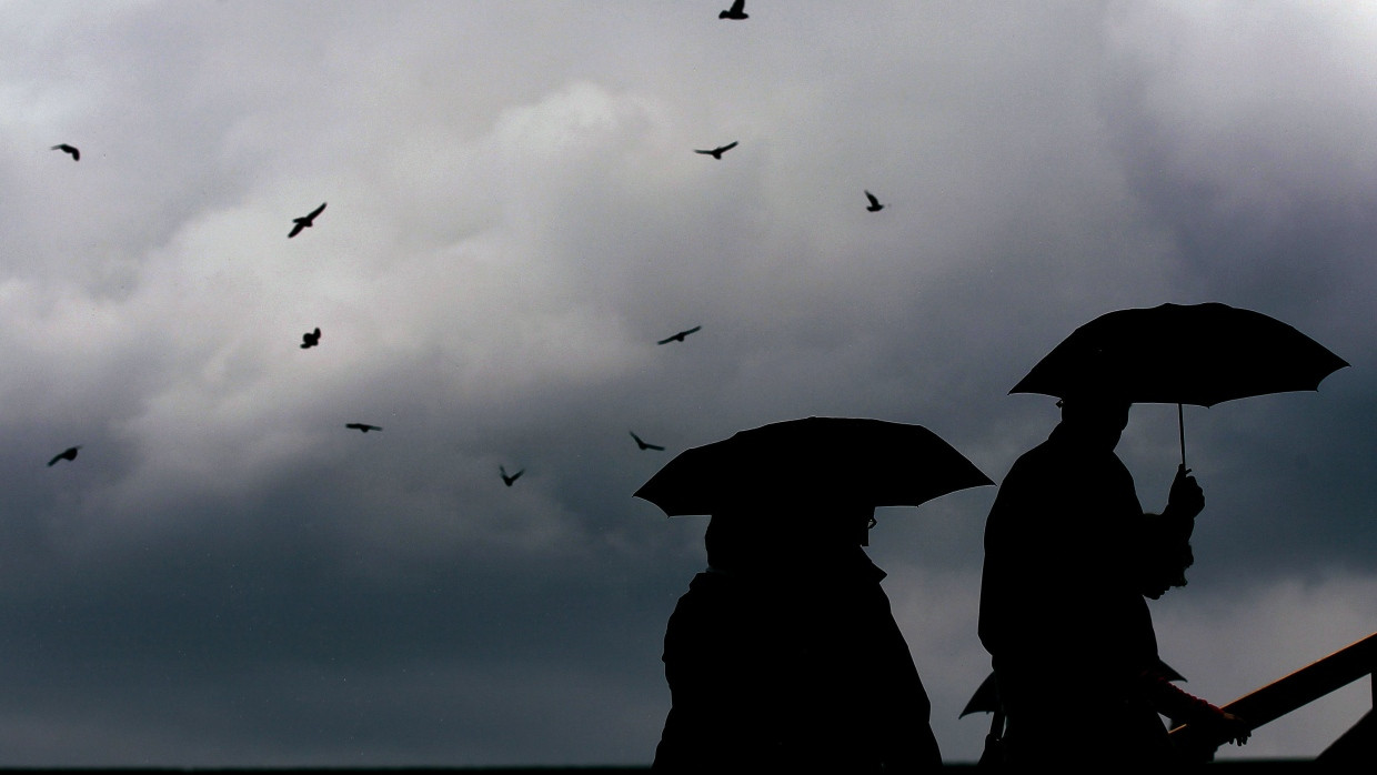 Fußgänger schützen sich mit Regenschirmen vor einem sich anbahnenden Unwetter (Symbolbild).