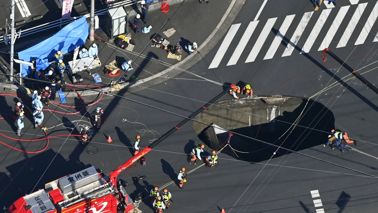 Einsatzkräfte beugen sich am Dienstag in der japanischen Stadt Yashio über das riesige Erdloch, in das ein Muldenkipper gestürzt ist.