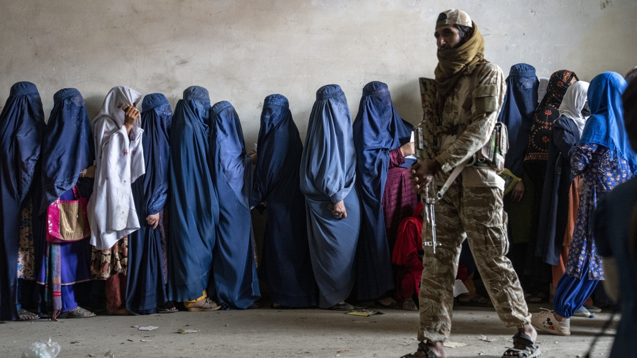 Ein Taliban-Kämpfer steht Wache, während Frauen in Kabul darauf warten, Lebensmittelrationen zu erhalten, die von einer humanitären Hilfsgruppe verteilt werden.