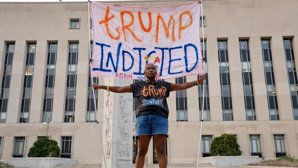 „Trump angeklagt - immer und immer wieder“ - Eine Demonstrantin hält am Dienstag ein Banner vor dem Gerichtsgebäude in Washington in die Höhe, in dem Donald Trump wegen Wahlbeeinflussung angeklagt wird.