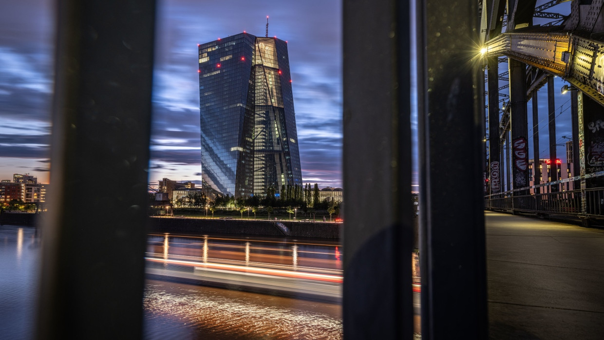 Die Zentrale der Europäischen Zentralbank (EZB) steht im Abendlicht hinter einem Geländer der Deutschherrnbrücke in Frankfurt.