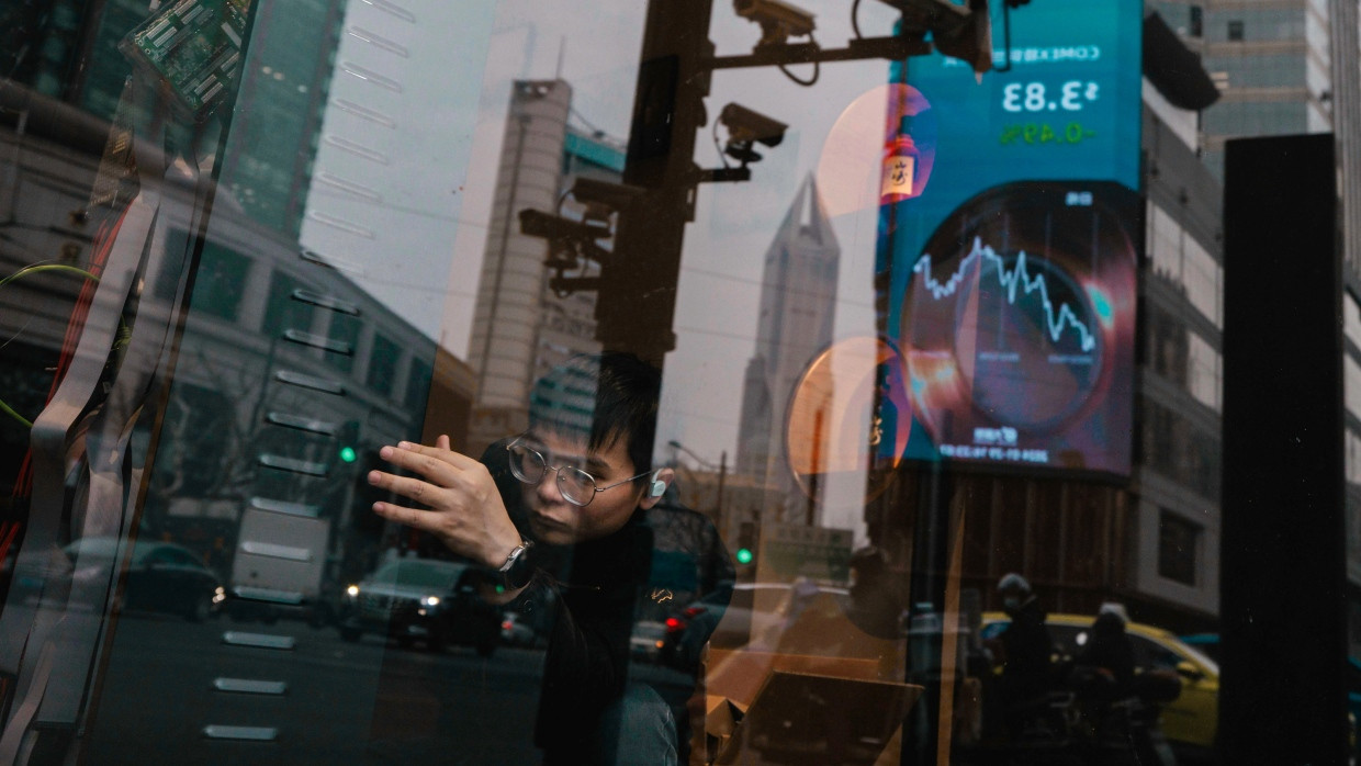 Ein Mann arbeitet in einem Geschäft in Shanghai, in dessen Schaufenster sich aktuelle Börsen- und Wirtschaftsdaten spiegeln. (Archivbild)