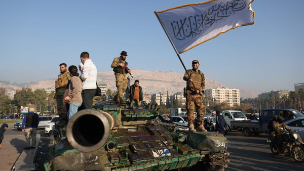 Menschen feiern am 9. Dezember auf einem zurückgelassenen Panzer in Damaskus den Sturz Assads.