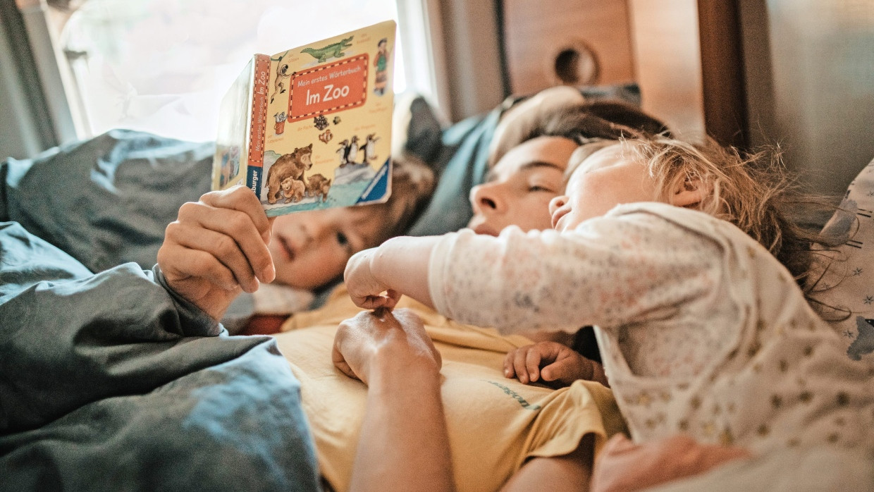 In großer Nähe: Eine Mutter liest ihren Kindern auf dem Bett eines Wohnmobils liegend vor.