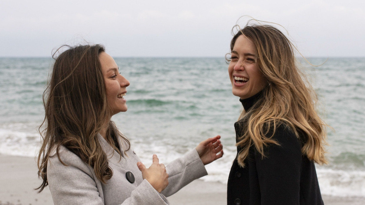 Zwei Freundinnen stehen gemeinsam am Meer und lachen. (Symbolbild)