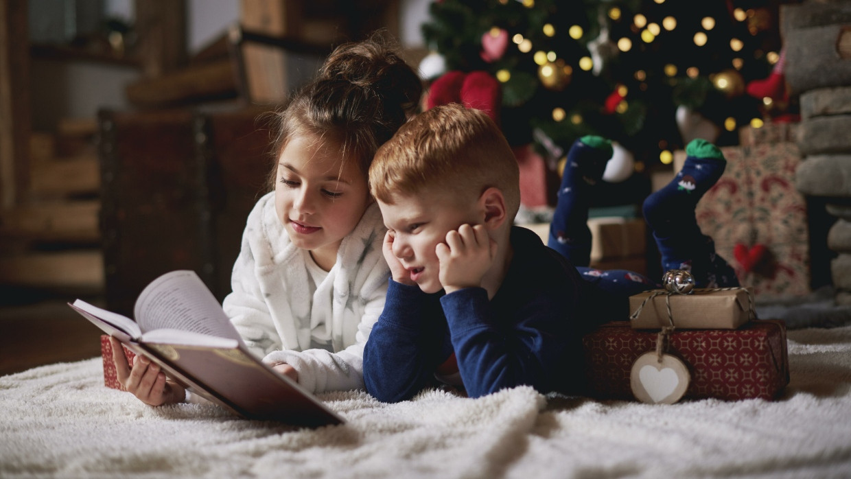 Geschwister lesen unter einem Weihnachtsbaum. (Symbolbild)