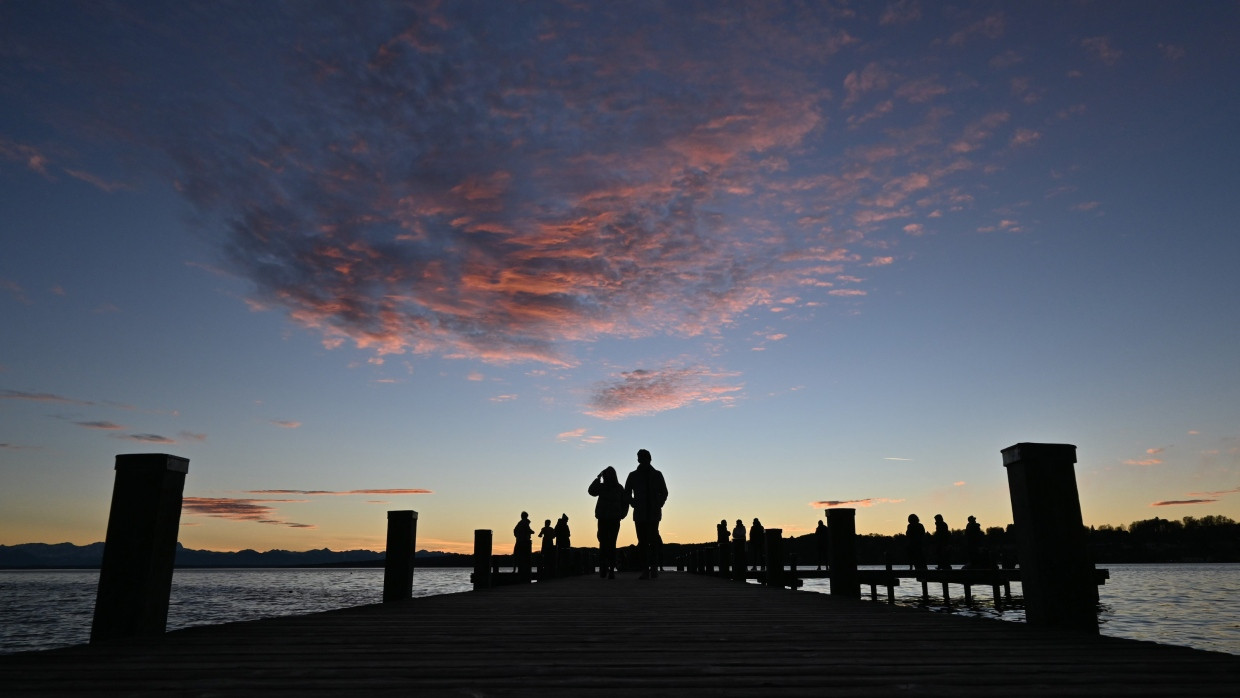 Ein Pärchen geht bei Sonnenuntergang am Silvesterabend über einen Steg am Starnberger See.