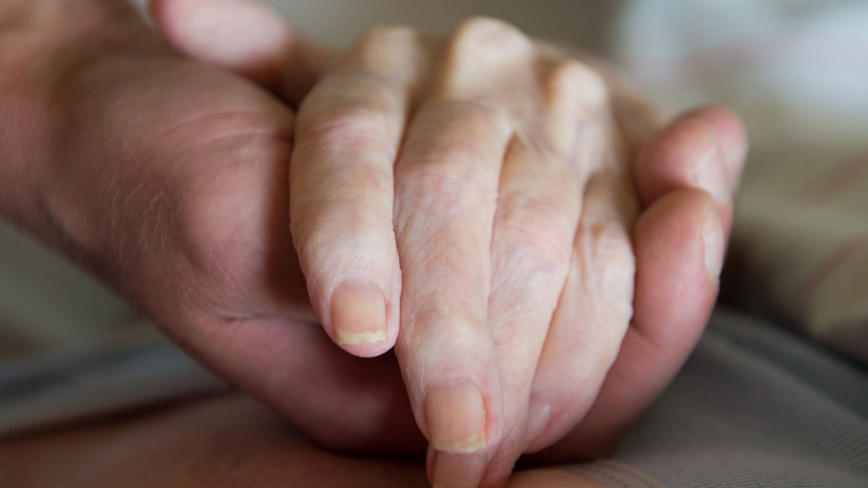 Ein Altenpfleger hält in einem Pflegeheim die Hand einer Frau (Symbolbild).