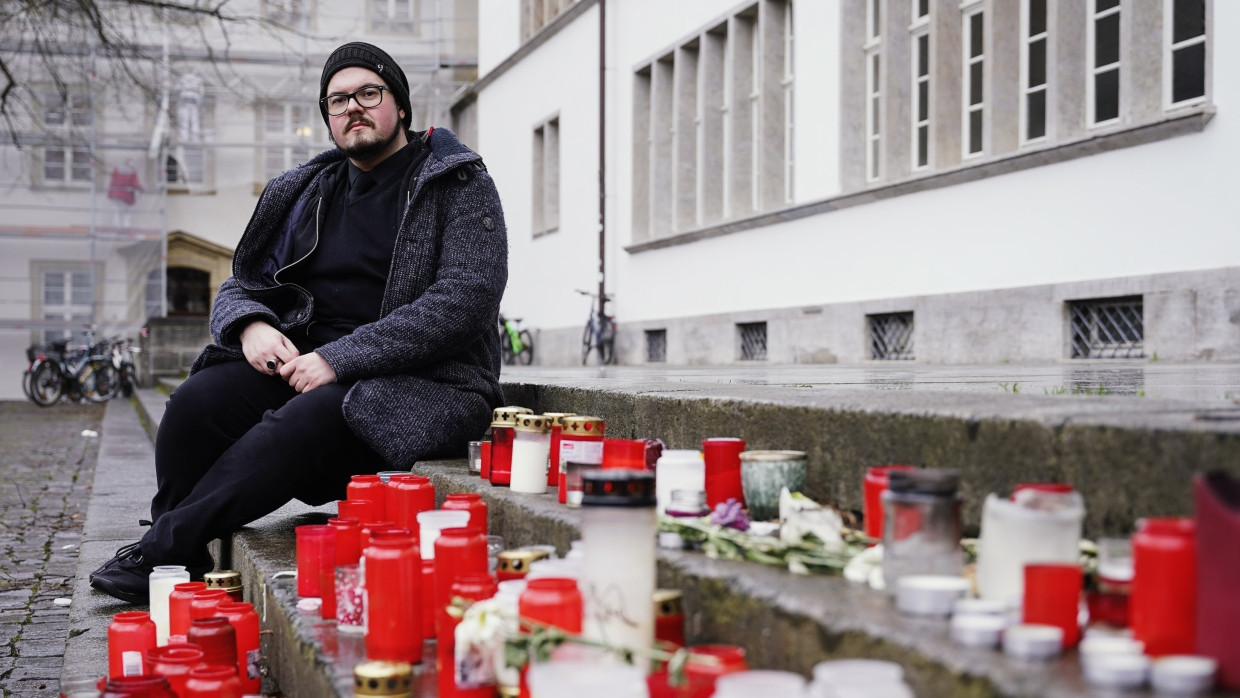 Peter Abelmann, Vorsitzender der Verfassten Studierendenschaft der Universität Heidelberg, sitzt vor Beginn eines Trauerzugs für die Opfer des Heidelberger Amoklaufs neben niedergelegten Blumen und Kerzen am Gebäude der Neuen Universität.