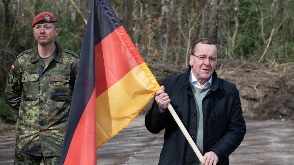 Boris Pistorius hält auf dem Gelände eines geplanten Bundeswehrstandorts eine Deutschlandfahne.