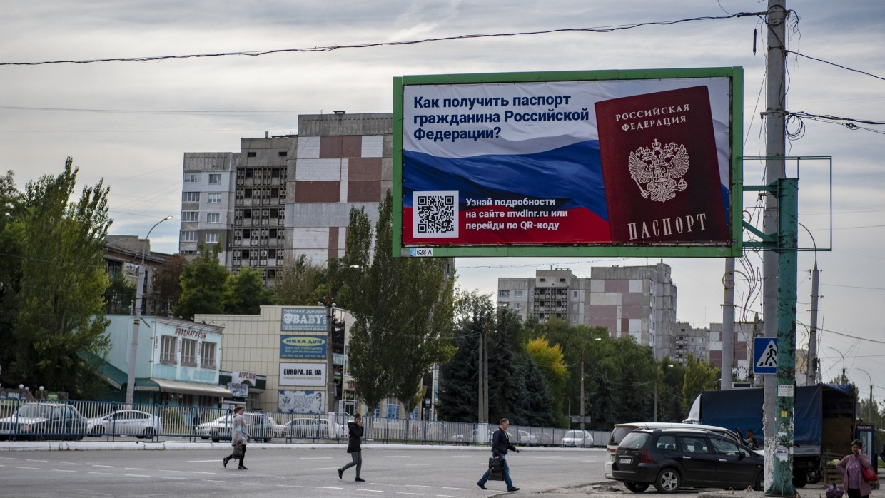 Ukraine, Luhansk: Menschen überqueren eine Straße mit einem Plakat mit der Aufschrift „Wie man den Pass eines russischen Bürgers bekommt".