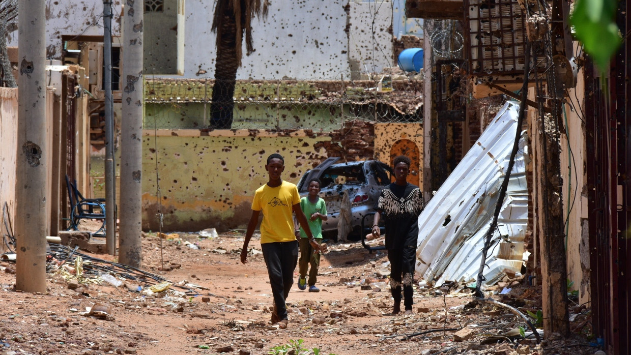 Sudan, Omdurman: Jugendliche gehen auf einer von Zerstörungen gezeichneten Straße. Im Sudan herrscht seit fast 16 Monaten ein blutiger Machtkampf. Der Konflikt hat die nach UN-Angaben weltweit größte Flüchtlingskrise ausgelöst.