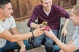 Three men holding drinks smile and toast