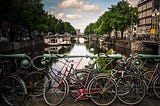 A view of an Amsterdam canal with several vintage bicycles in the foreground.