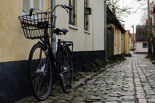 A vintage bycicle painted in black parked next to a yellow house.