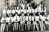 a group of school girls sit, with hands on laps.