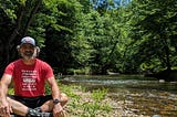 The author sitting crosslegged on a bed of rocks by a shallow creek.