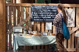 A man standing in front of a table with bakery goods and making an honor payment of their purchase.