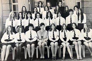 a group of school girls sit, with hands on laps.