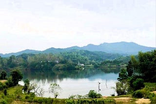 The road the author used to walk with their grandmother runs by a river with mountains in the background.