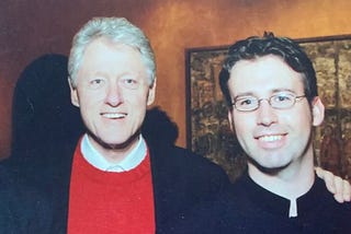 Former president Bill Clinton stands next to a young man with glasses