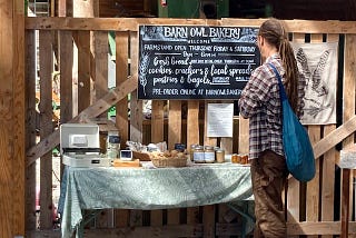 A man standing in front of a table with bakery goods and making an honor payment of their purchase.