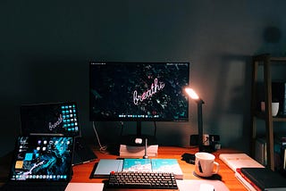 An image of a desk with a monitor, computer, and an iPad with lights shining on a coffee cup.