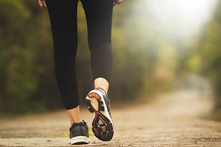 Lady wering black leggingsd and trainers walking along a leafy lane in sunlight, only her legs visible in the image.