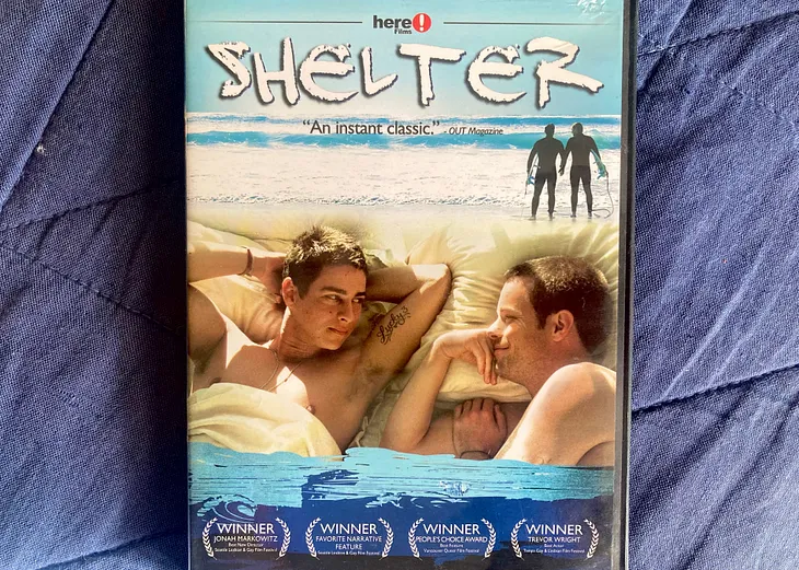 The DVD of the movie Shelter, featuring two men staring at one another while in bed, with an image of two men facing the ocean above them