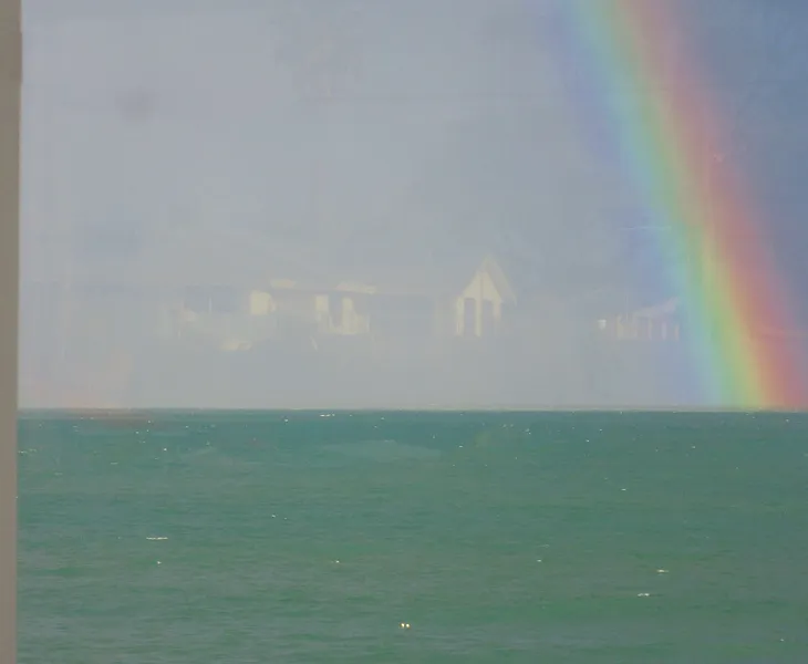 Image of a rainbow a green ocean with a reflection of houses in the sky