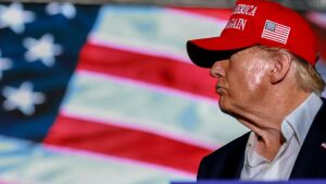 Former President Donald Trump speaks at a campaign rally at the Trump National Doral Golf Club in Florida on July 9. The photo shows a side profile of his head, directed to the left. Trump is wearing a red baseball cap with an American flag embroidered on it. An American flag is in the background.