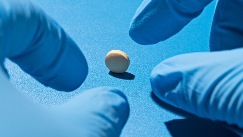 Blue Medical Gloved Hand About to Pick up a Yellow Pill on Blue Background Close-up View.