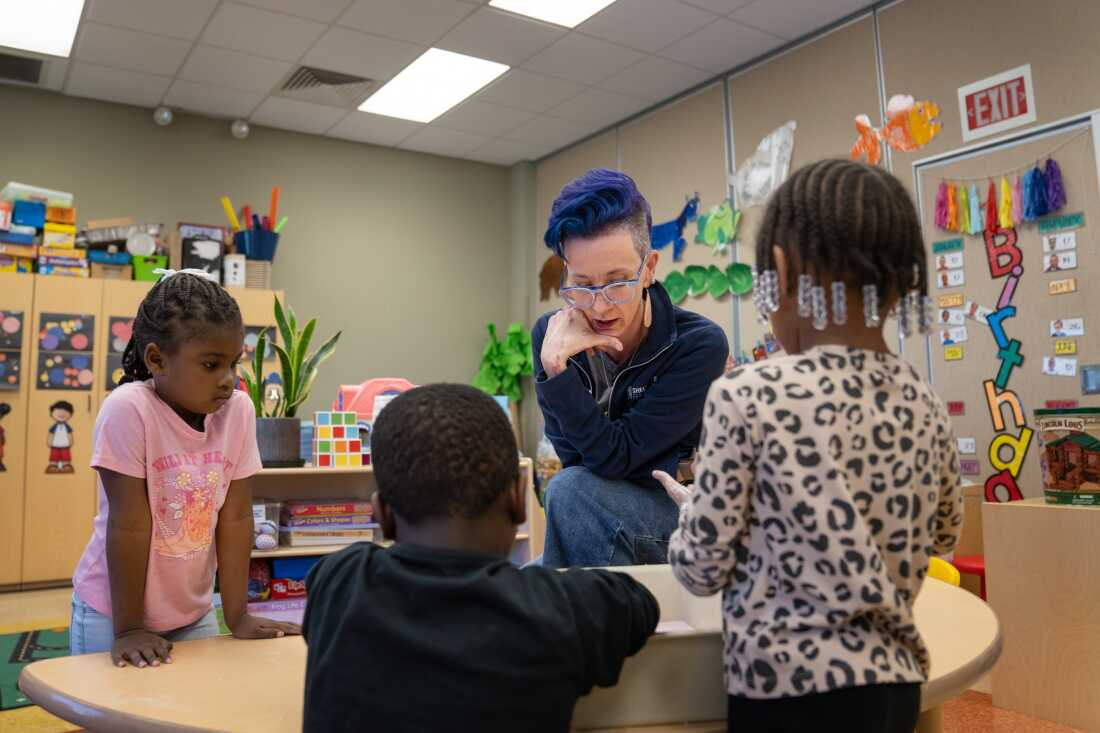 Holly Glasgow sits at a table with three children in the pre-K program she directs on the campus of Shelton State Community College in Tuscaloosa.