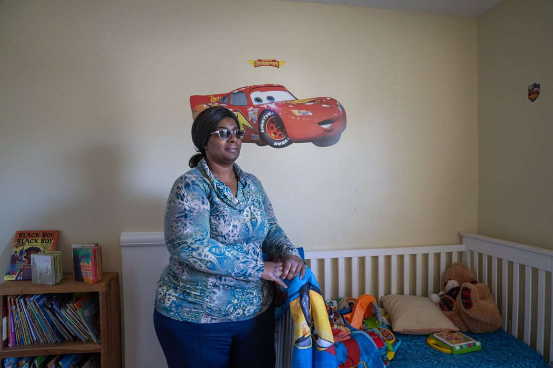 Lakethia Clark stands between a bookcase full of children's books and a toddler bed.