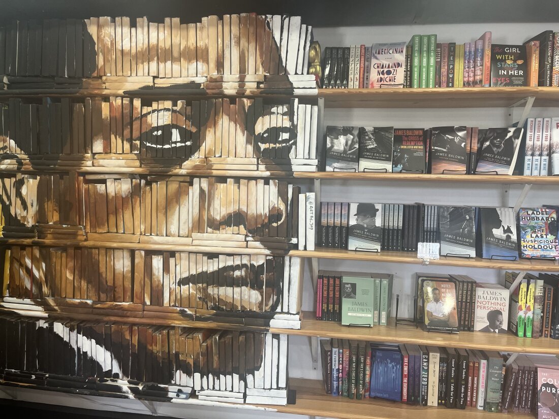 On the left side of this photo, James Baldwin's face is painted on a decorative bookcase inside the Baldwin & Co. bookstore in New Orleans. On the right are books arranged on rows of bookshelves.