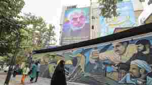 People walk past a billboard showing a portrait of Hamas leader Yahya Sinwar (top) next to Palestine Square in the Tehran on Aug. 12, 2024.