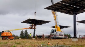 A cherry picker and a small crane in a field full of solar panels lifted on metal stands a could feet off the ground. 