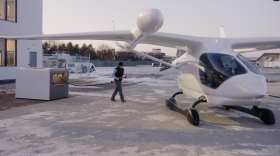 A man walks over to a small white aircraft with a charging cord from a charging station. 