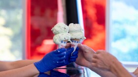 Hands reach across a glass counter towards two ice cream cones.