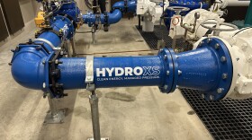 The curved blue pipe that holds a micro-hydropower turbine is shown inside a pumphouse at Skagit PUD, with the logo 'HydroXS' painted in it in white.