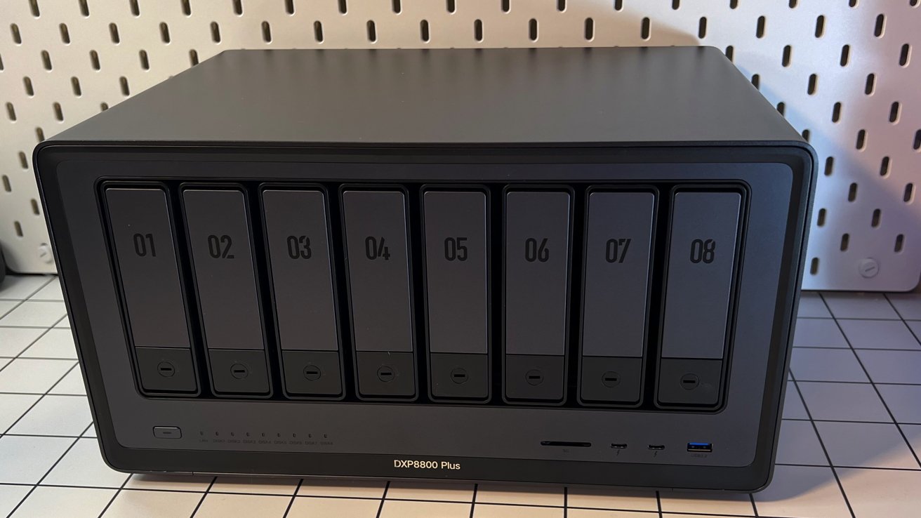 A black Ugreen network attached storage device with eight bays labeled 01 to 08 and status lights on a checkered surface.